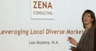 Picture of woman standing and smiling. Brown hair, white skin, holding a pencil and in front of a white board that has words on it, ZENA CONSULTING, Leveraging Local Diverse Markets, Lee Mozena, M.A.. T d.